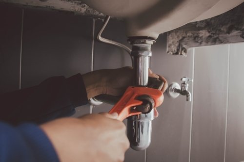 Plumber using a wrench to tighten a sink drain pipe, demonstrating plumbing repair services relevant to Great American Plumbing's offerings in Coral Springs.