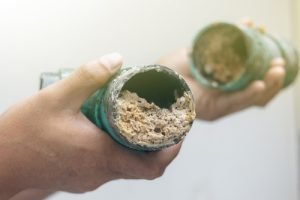 Hands holding two clogged plumbing pipes filled with debris, illustrating plumbing issues relevant to Great American Plumbing's services in Southwest Ranches.