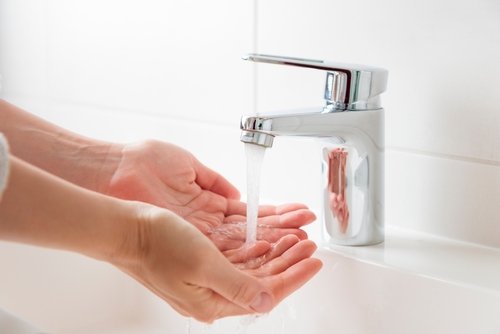 Hands under a modern faucet with running water, illustrating effective plumbing solutions and water usage practices.