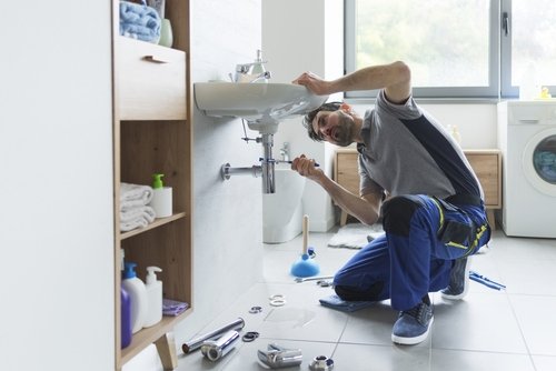 Plumber repairing a sink in a modern bathroom, surrounded by plumbing tools and supplies, representing Great American Plumbing's expert services and plumbing tips.