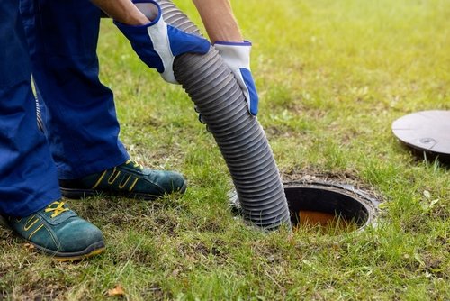 Plumber using a vacuum hose to clean a septic tank, emphasizing proper maintenance for wastewater management in residential plumbing.